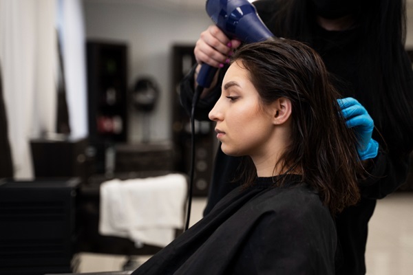 Formaldehído para alisar el pelo - Estilista usando un secador de pelo para eliminar el exceso de humedad y alisar el cabello de una mujer