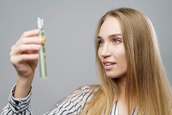 Formaldehído para alisar el pelo - Mujer con el cabello liso y de color rubio sosteniendo en su mano una ampolla para los tratamientos de queratina