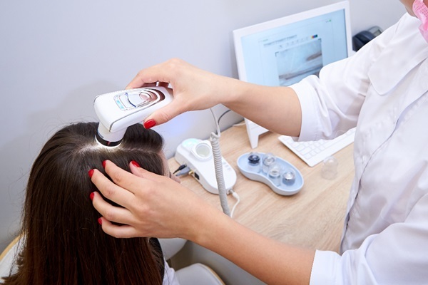 Láser de baja potencia - Tricólogo aplicando un tratamiento con láser de baja intensidad en el cuero cabelludo de una mujer para fortalecer el cabello