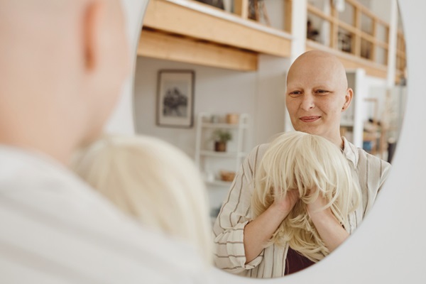 Pérdida de cabello por quimioterapia - Mujer frente al espejo sosteniendo en su mano una peluca para disimular la caída del pelo por quimioterapia contra el cáncer