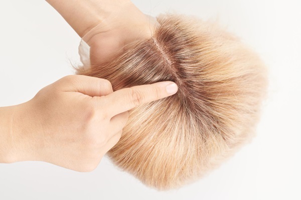 Prótesis capilar técnica FAS - Hombre sosteniendo en su mano una prótesis de cabello natural de color rubio para recuperar el pelo perdido por enfermedades del cuero cabelludo