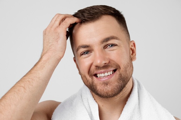 Añadir volumen al cabello fino - Hombre feliz tocando su cabello con volumen gracias a los consejos para conseguir un cabello más voluminoso