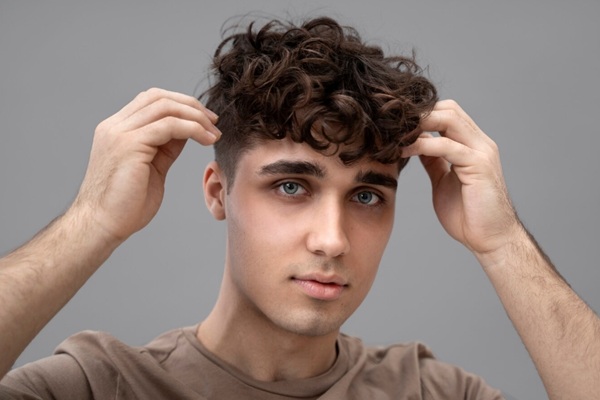 Añadir volumen al cabello fino - Hombre joven aprendiendo cómo aumentar la densidad del pelo fino al ondular o rizar el cabello