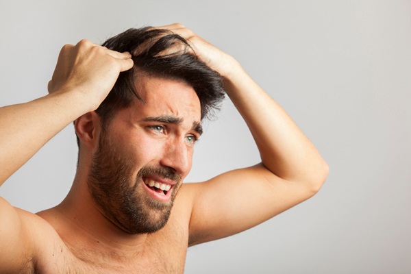 Cabello grasoso - Hombre con cara de preocupación tocando su pelo grasoso que puede causar afecciones en el cuero cabelludo y la caída del cabello
