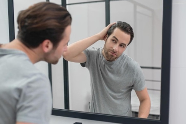 Errores en el cuidado del cabello - Hombre observando en el espejo los beneficios de una  rutina de cuidados para embellecer el cabello con el uso correcto de champú y acondicionador
