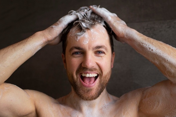 Errores en el cuidado del cabello - Hombre siguiendo una rutina de cuidado capilar lavando su pelo con abundante champú sin productos químicos para proteger el cabello
