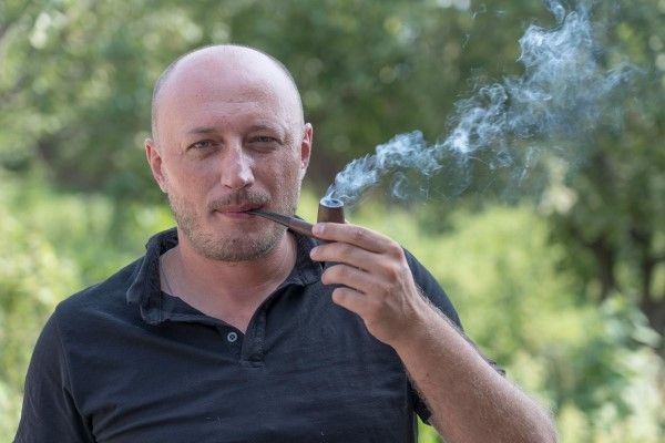 Tabaco y alopecia - Hombre con pérdida de cabello avanzada fumando tabaco en un parque que afecta la salud capilar y general