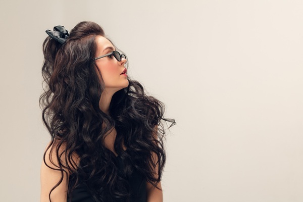 Tipos de cabello ondulado - Mujer joven posando de perfil con su cabello ondulado sin encrespamiento gracias al uso de productos capilares que reducen la porosidad del cabello