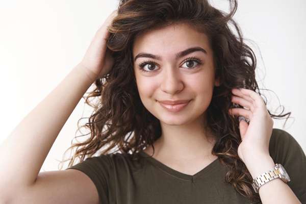 Tipos de cabello ondulado - Mujer colocando las manos en su cabello con ondas sin frizz gracias a una correcta hidratación capilar