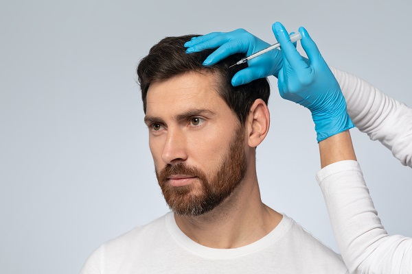 Médico capilar aplicando un tratamiento en el cuero cabelludo de un hombre para estimular el crecimiento del cabello