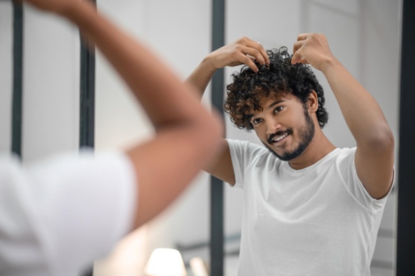 Trasplante cabello rizado - Hombre feliz tocando su pelo rizado abundante gracias al trasplante cabello CDMX