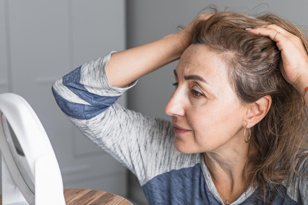 Calvicie en mujeres - Mujer observando frente al espejo la presencia de varios tipos de alopecia que ocasionan la caída del cabello en la línea frontal